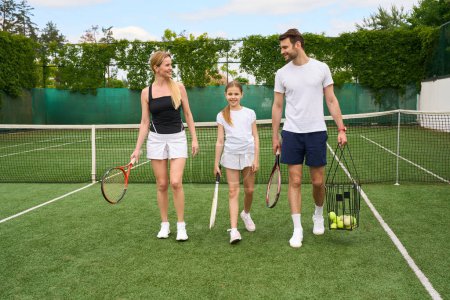 Foto de Papá, mamá y la hija adolescente están caminando por la cancha de tenis, tienen raquetas de tenis en sus manos - Imagen libre de derechos