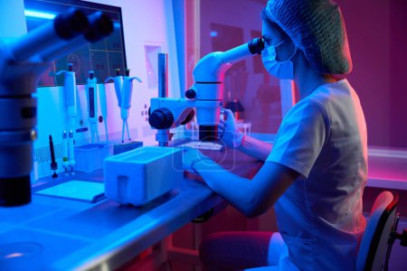 Foto de Embrióloga femenina trabaja con biomaterial para la criopreservación, utiliza el conjunto de micromanipuladores y el tanque de nitrógeno líquido - Imagen libre de derechos