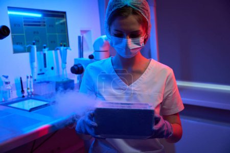 Téléchargez les photos : Femme embryologue tient un réservoir avec de l'azote liquide dans ses mains pour la cryoconservation de matériel biologique - en image libre de droit