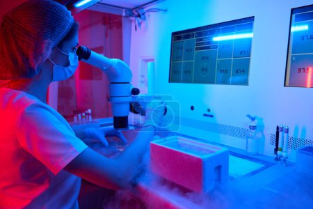 Photo for Laboratory assistant embryologist at work in the cryo-laboratory, on the table a tank with liquid nitrogen - Royalty Free Image