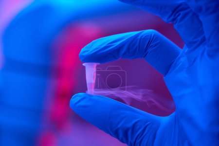 Téléchargez les photos : Assistant de laboratoire dans des gants de protection tient une petite éprouvette avec biomatériau à la main, conditions optimales dans le laboratoire - en image libre de droit