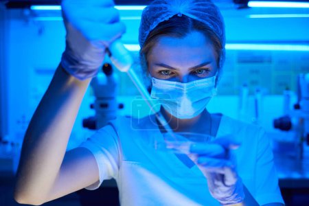 Photo for Embryologist in a protective mask manipulates the biomaterial, she uses a petri mug and a special pipette - Royalty Free Image