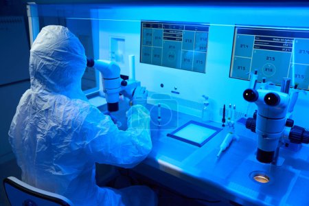 Téléchargez les photos : Travailleur de laboratoire dans un uniforme de protection effectue une biopsie des embryons, il utilise le micromanipulateur et un microscope puissant - en image libre de droit