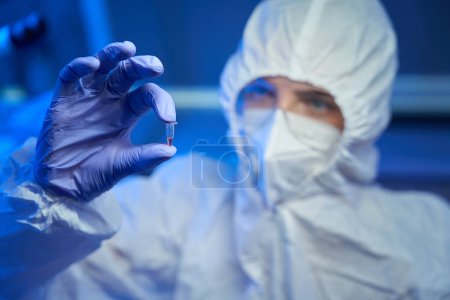 Téléchargez les photos : Un assistant de laboratoire en uniforme stérile tient une éprouvette avec un biomatériau dans les mains - en image libre de droit