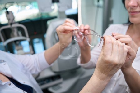 Photo for Cropped photo of optician giving new pair of eyeglasses to adult woman - Royalty Free Image