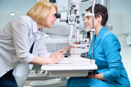 Téléchargez les photos : Ophtalmologiste focalisé regardant à travers le microscope de lampe à fente aux yeux des patientes - en image libre de droit