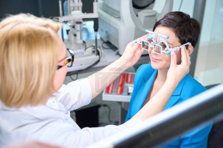Photo for Oculist putting on trial frame with polarizing filters on smiling female patient face - Royalty Free Image