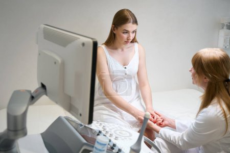 Téléchargez les photos : Médecin féminin communique chaudement avec une jeune femme dans la salle d'échographie, le médecin tient les mains des patients - en image libre de droit