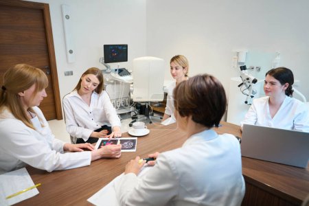 Foto de El médico muestra a la mujer joven imágenes de ultrasonido, los médicos y la paciente están sentados en una mesa grande - Imagen libre de derechos