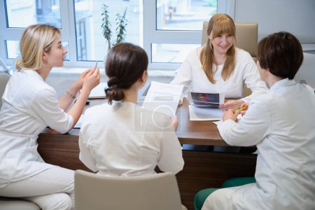 Photo for Women doctors in medical uniforms gathered for a medical consultation, they study the working material - Royalty Free Image