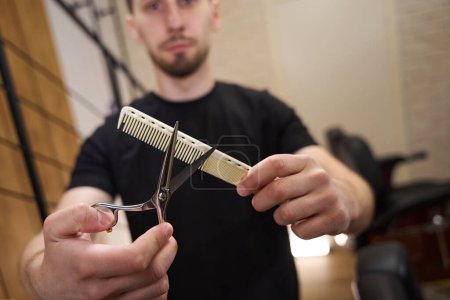 Foto de Peluquero sostiene tijeras especiales y un peine en sus manos, un interior minimalista en una barbería - Imagen libre de derechos