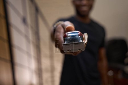 Photo for African American barber holds a special electric razor in his hands, the guy is at the workplace in the barbershop - Royalty Free Image