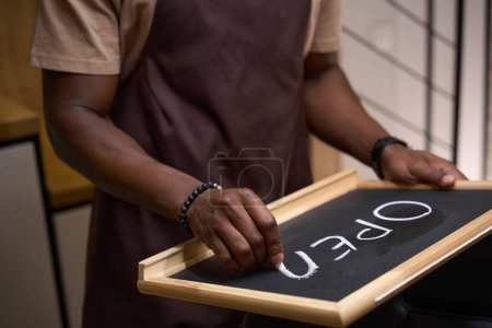 Photo for Young man writes in chalk on a sign open, the room is clean and bright - Royalty Free Image