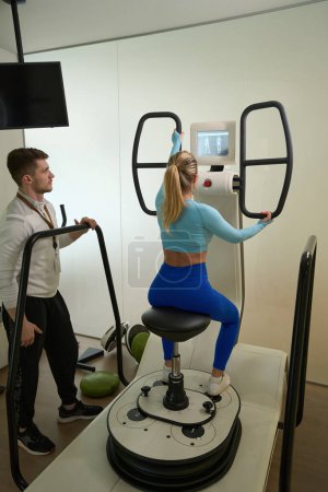 Foto de Mujer delgada en ropa deportiva haciendo ejercicios mientras su entrenador la observa en la habitación moderna - Imagen libre de derechos