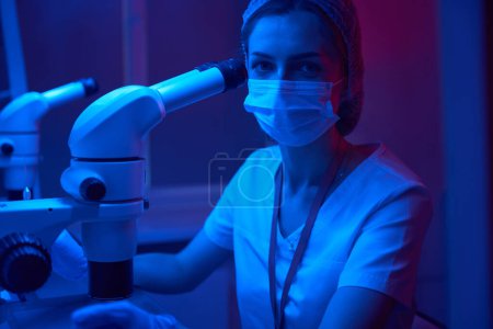 Photo for Young laboratory assistant at workplace in cryolab, female uses powerful microscope - Royalty Free Image