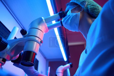 Photo for Woman uses a powerful microscope in her work, she is in the workplace in a modern laboratory - Royalty Free Image
