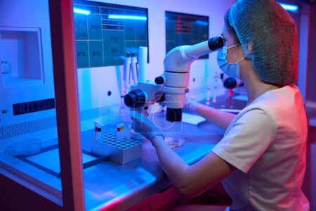 Foto de Embrióloga utiliza un potente microscopio en su trabajo, ella está en el lugar de trabajo en un laboratorio moderno - Imagen libre de derechos