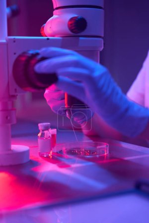Scientifique embryologue travaille avec biomatériau, un spécialiste ajuste l'oculaire avec une main dans un gant de protection