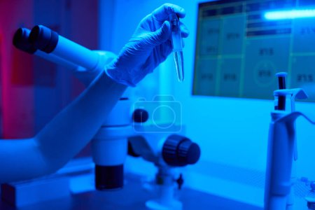 Foto de Embriólogo sostiene un tubo de ensayo con biomaterial en la mano, en el potente laboratorio de microscopio - Imagen libre de derechos