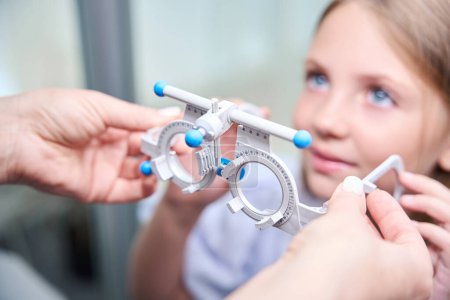 Photo for Closeup of ophthalmologist hands putting ophthalmic trial frame on little girl face - Royalty Free Image