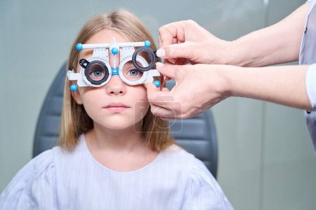 Foto de Oculista insertando lentes esféricas en células de marco de ensayo oftálmico en la cara joven del paciente - Imagen libre de derechos