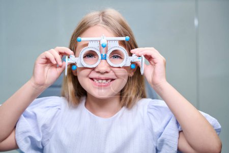 Portrait of cheerful little girl with ophthalmic trial frame on face looking in front of her