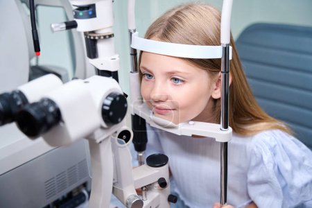 Photo for Child holding her head against chinrest and forehead support during slit lamp examination - Royalty Free Image