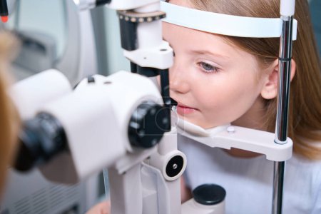 Photo for Tranquil pediatric patient undergoing slit lamp examination carried out by professional oculist - Royalty Free Image