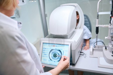 Augenoptikerin beim Betrachten des Augenbildes eines pädiatrischen Patienten auf Autorefraktor-Touchscreen