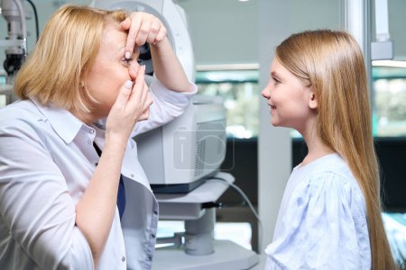 Photo for Orthoptist inserting contact lens into her eye in front of smiling pediatric patient - Royalty Free Image
