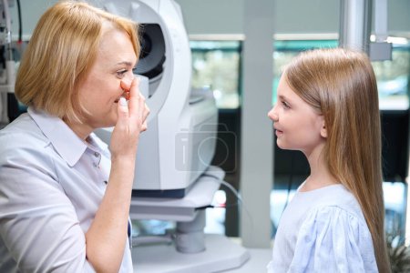 Téléchargez les photos : Vue latérale de l'ophtalmologiste mettant la lentille de contact dans son oeil avant la petite fille concentrée - en image libre de droit