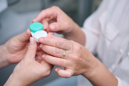 Cropped photo of female optometrist hands presenting contact lens storage case to patient