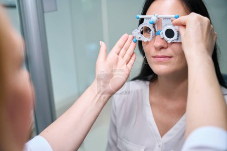 Foto de Optometrista insertando lente oclusiva en la celda del marco de ensayo frente al ojo izquierdo del cliente - Imagen libre de derechos