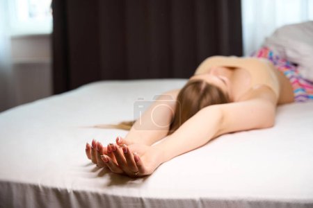 Téléchargez les photos : Photo de jeune femme en soutien-gorge et avec une belle manucure couchée sur le lit à l'intérieur - en image libre de droit
