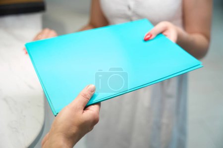 Photo for Employee of the clinic gives the patient a folder with documents, the ladies are at the reception - Royalty Free Image