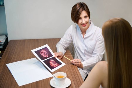 Téléchargez les photos : Deux femmes regardent ensemble des images d'échographie foetale, les femmes communiquent chaleureusement sur une tasse de thé - en image libre de droit