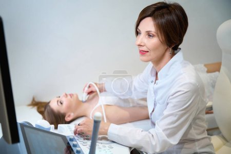 Téléchargez les photos : Médecin uzist effectue un examen de la glande thyroïde d'une jeune femme, le spécialiste utilise un équipement moderne - en image libre de droit