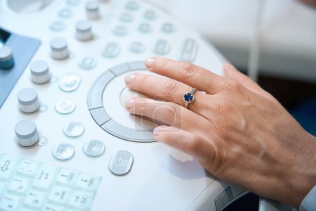 Téléchargez les photos : Uzist travaille sur une machine ultrasonore moderne, sa main avec un petit anneau sur le panneau de commande - en image libre de droit