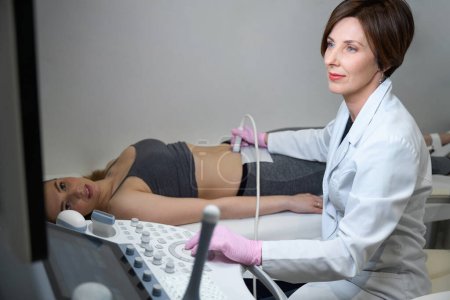 Téléchargez les photos : Docteur effectue une procédure d'échographie du fœtus d'une femme enceinte, dans la salle d'échographie il y a un appareil moderne - en image libre de droit