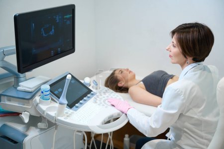 Téléchargez les photos : Uzist effectue une procédure d'échographie du fœtus d'une femme enceinte, une femme regarde l'écran avec un sourire - en image libre de droit