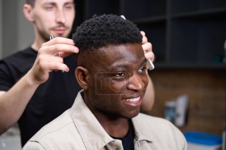 Foto de Afroamericano en una peluquería recibe consejos de un peluquero, el estilista tiene una herramienta de trabajo en sus manos - Imagen libre de derechos