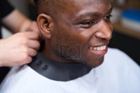 Photo for Barber puts a protective cape on a cute client, the guy has curly hair - Royalty Free Image