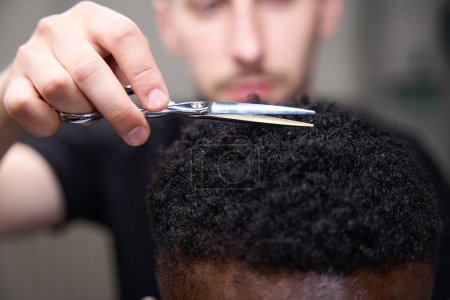 Téléchargez les photos : Styliste coupe les cheveux bouclés du gars afro-américain, l'homme utilise des ciseaux - en image libre de droit