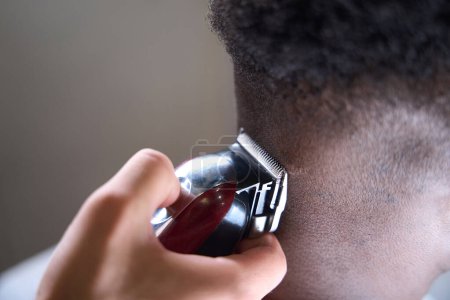 Téléchargez les photos : Coiffeur utilise une tondeuse moderne pour bordure sur l'arrière de sa tête, son client afro-américain a les cheveux bouclés - en image libre de droit
