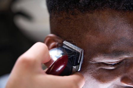 Foto de Estilista utiliza un moderno clipper para el ribete, su cliente afroamericano tiene el pelo rizado - Imagen libre de derechos