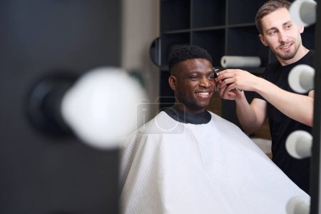 Foto de Master corta al cliente frente al espejo en la barbería, el espejo está equipado con lámparas especiales - Imagen libre de derechos