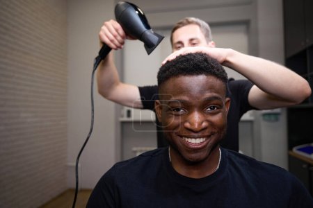Photo for Hairdresser dries African American males hair, the master uses a professional hair dryer - Royalty Free Image