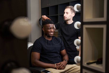 Téléchargez les photos : Coiffeur devant le miroir fixe les cheveux des clients afro-américains, le maître utilise un peigne spécial - en image libre de droit