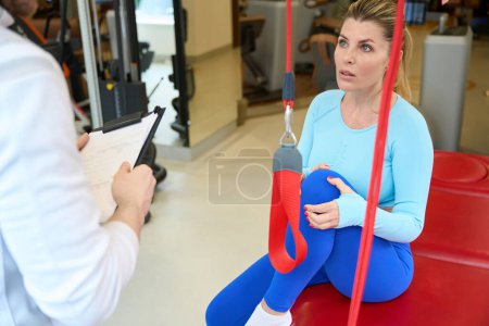 Photo for Caucasian woman with long hair preparing for exercises and looking at her instructor in modern room - Royalty Free Image