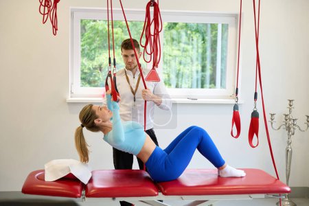 Photo for Beautiful female client doing suspension exercises with trainer by using redcord indoors - Royalty Free Image